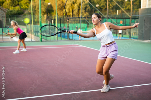 Young beautiful sportswoman in white t-shirt and shorts playing tennis on open summer court. Racket sport training outdoors © JackF