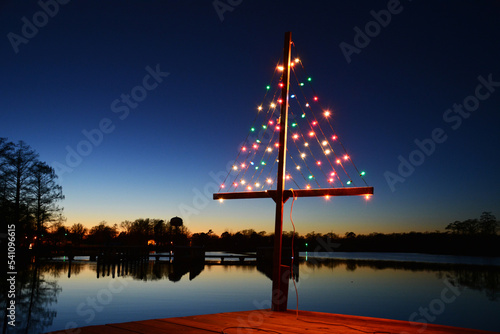 Christmas lights in the shape of a tree placed on the end of a dock at sunset.