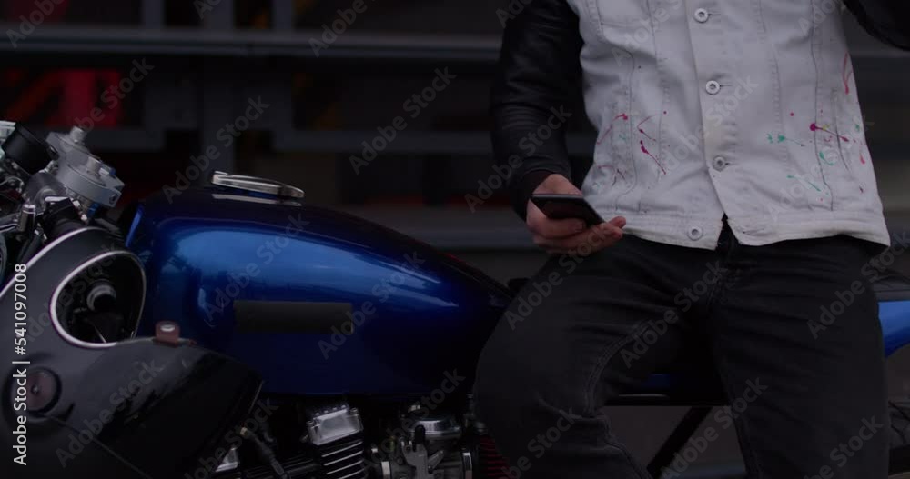 Close-up of a motorcyclist sitting on a motorcycle writing a text on a smartphone watching the news. Biker drinking coffee flipping through social networks in the phone sending a message Close-up of a motorcyclist sitting on a motorcycle writing a text on a smartphone watching the news. Biker drinking coffee flipping through social networks in the phone sending a message