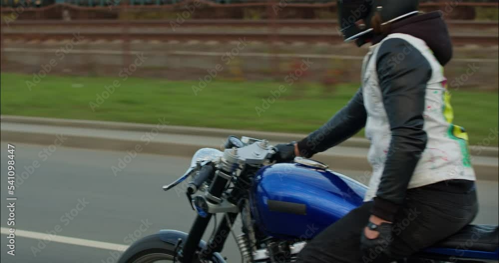 Driving Bike on Streets. Biker riding his custom built cafe racer motorcycle and showing joyful hand gestures. Happy motorcyclist riding on a city road with great speed. Side view. . Driving Bike on Streets. Biker riding his custom built cafe racer motorcycle and showing joyful hand gestures. Happy motorcyclist riding on a city road with great speed. Side view. .