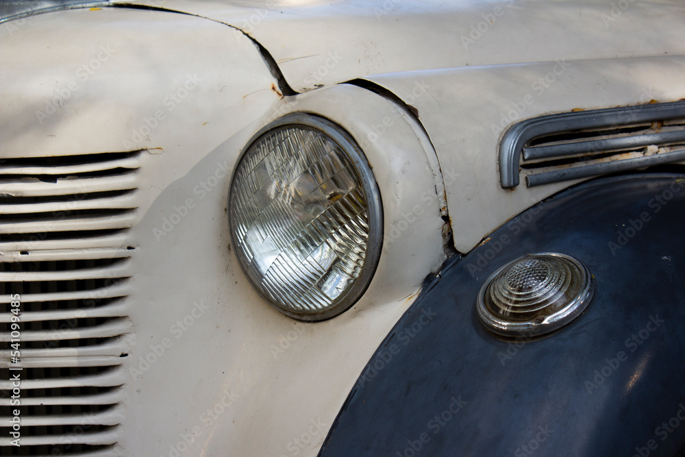 Photo of a fragment of a vintage old retro car with round headlights. The hood and fender of the car. Crisis in the car market. The concept of obsolescence and antiques.