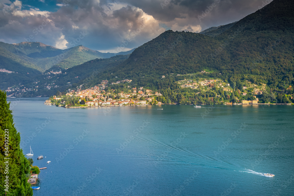 Idyllic Lake Como coastline with village and sailboat at dramatic sunset, Italy