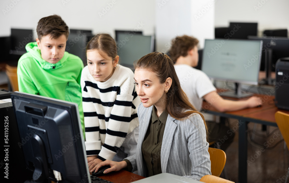 Fototapeta premium Interested teenagers studying with young female teacher in information technology class at college, sitting around one computer
