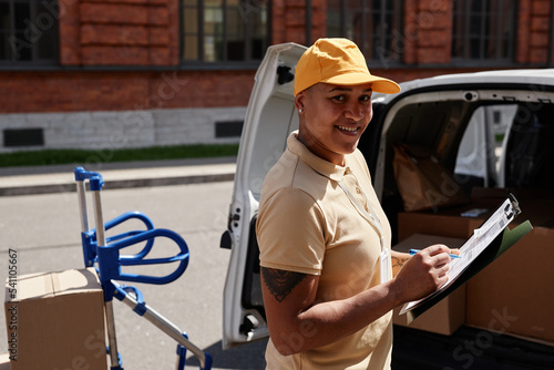 Waist up portrait of multiethnic young woman unloading van with packages and smiling at camera