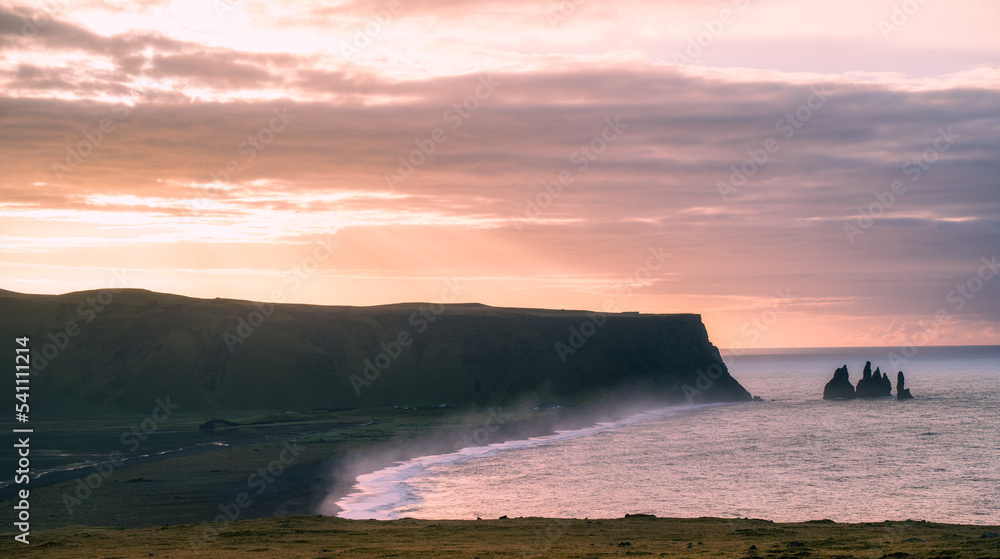 sunrise over the sea at the Dyrhólaey with clouds, cliff and water splash