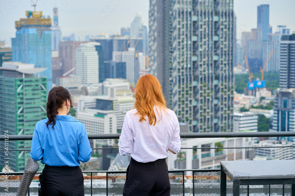 Two Businesswoman are talking and looking view of cityscape on rooftop building