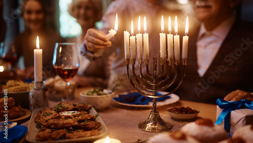 Close up of boy lights candles in menorah while celebrating Hanukkah with his family at dining table. photo