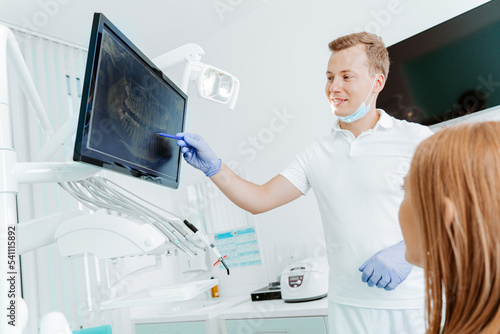Doctor dentist and woman patient watching x-ray on digital screen in stomatology clinic with medical equipment. Smile healthy teeth concept