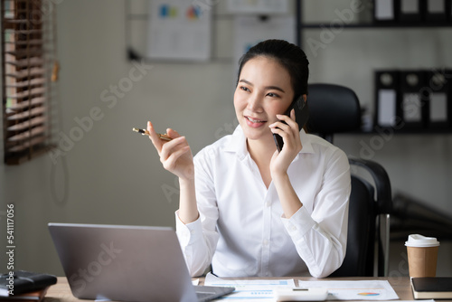 Cute asian woman having a cup of tea while using laptop computer in office