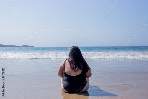 mujer sentada a la orilla del mar portando un traje de baño completo negro del mar levantando los brazos sosteniendo un letrero de globo con la palabra hello de color rosa photo