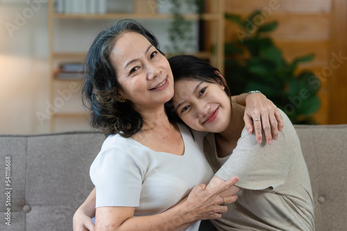 Happy senior Asian woman and her adult daughter are cuddling on the couch