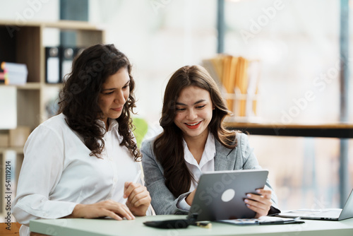 Young friendly business people are talking to each other, while sitting at the desk in a modern office. Focus on woman. Concept of business success