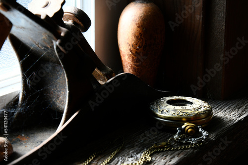 A beautiful gold colored vintage pocket watch resting on a wooden window ledge with dramatic lighting.  photo