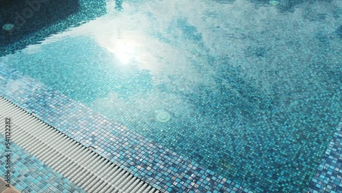 Sun glare in a beautiful swimming pool lined with blue mosaics. Clear blue water in the pool. Relax in the backyard of a country house
