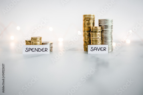 Saver vs spender texts in front of big and small stacks of coins. Concept  of money, abundance and wealth