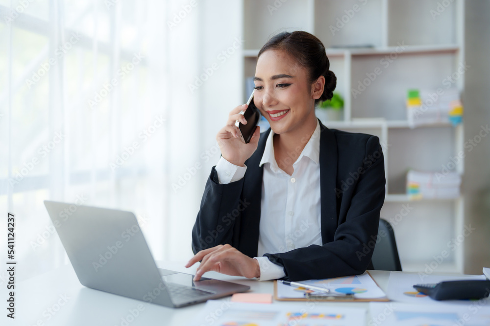 Beautiful Asian business woman chatting on the phone with customer and working on her laptop and taking note enthusiastically and happily in the office. Beautiful Asian business woman chatting on the phone with customer and working on her laptop and taking note enthusiastically and happily in the office.