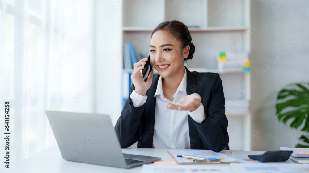 Beautiful Asian business woman chatting on the phone with customer and working on her laptop and taking note enthusiastically and happily in the office. Beautiful Asian business woman chatting on the phone with customer and working on her laptop and taking note enthusiastically and happily in the office.