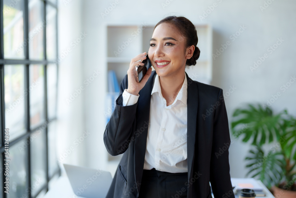 Beautiful Asian business woman chatting on the phone with customer and working on her laptop and taking note enthusiastically and happily in the office. Beautiful Asian business woman chatting on the phone with customer and working on her laptop and taking note enthusiastically and happily in the office.