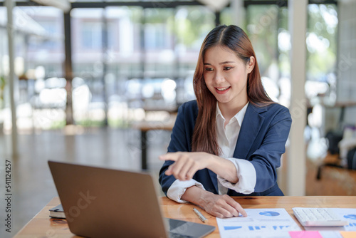 Portrait of smiling Asian business woman enjoying work ideas sitting on laptop at office.