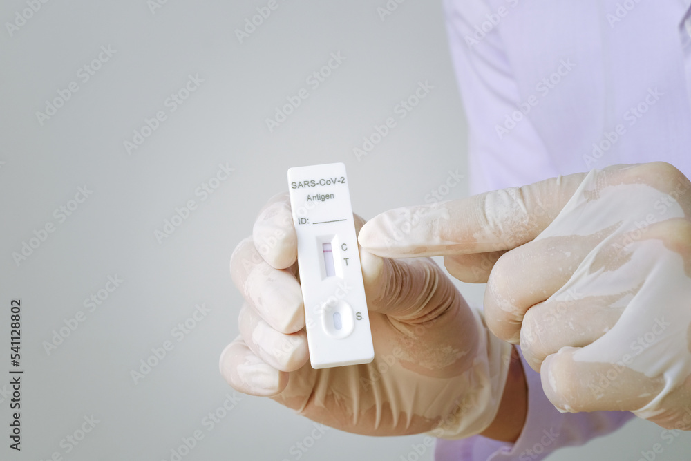 A doctor or nurse wearing rubber gloves holding a 1 red line Antigen Rapid Test kit (ATK) with negative results during a COVID-19 swab test.