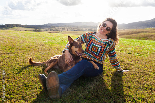 Companions - happy middle age woman and kelpie dog sitting together on farm hilltop