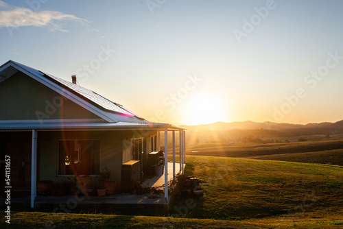 Homestead on hilltop with last rays of sunlight shining over scene and solar panels on roof