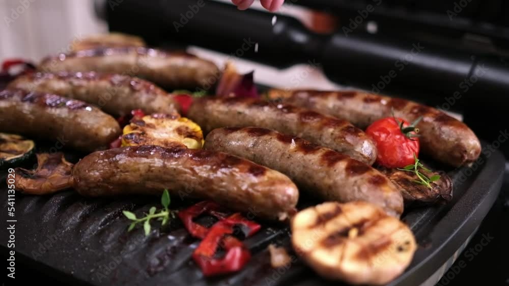 Homemade juicy pork sausages with spices and vegetables frying on electric grill Homemade juicy pork sausages with spices and vegetables frying on electric grill