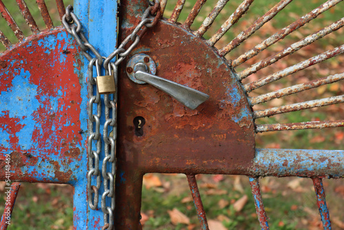 Close-up of blue and rusty old gates of are locked with chain and padlock around them.  Locked gate. No entry, restricted area