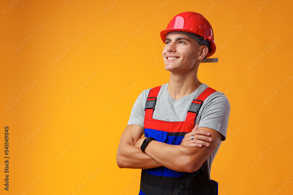 Young construction worker in helmet and uniform posing on yellow background in studio Young construction worker in helmet and uniform posing on yellow background in studio