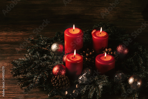 four burning Red advent candles in advent wreath decoration on wooden dark background. tradition in time before Christmas. xmas lights with christmas fir deco background concept. Festive still life.