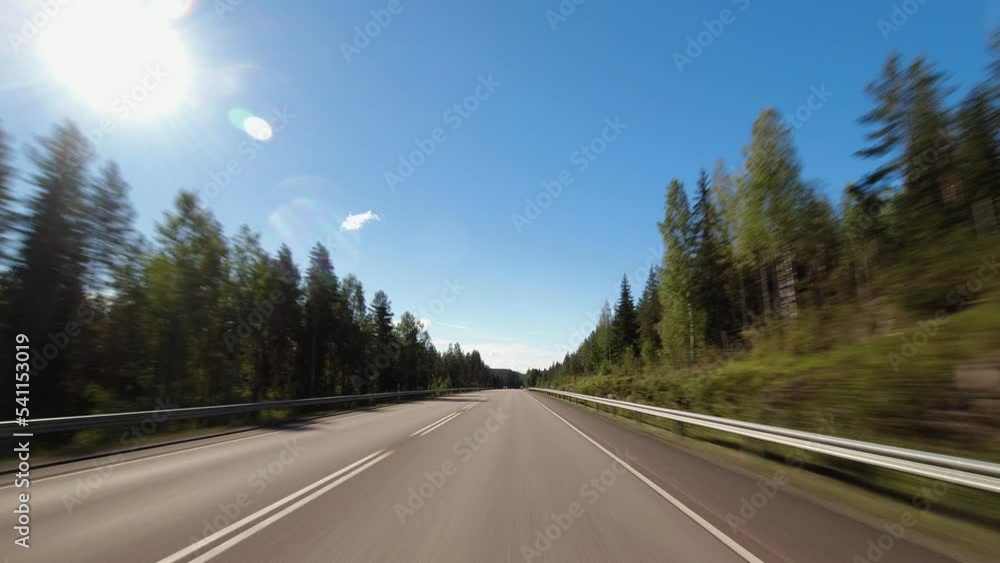 Blue sky driving POV on highway through northern evergreen forest Blue sky driving POV on highway through northern evergreen forest