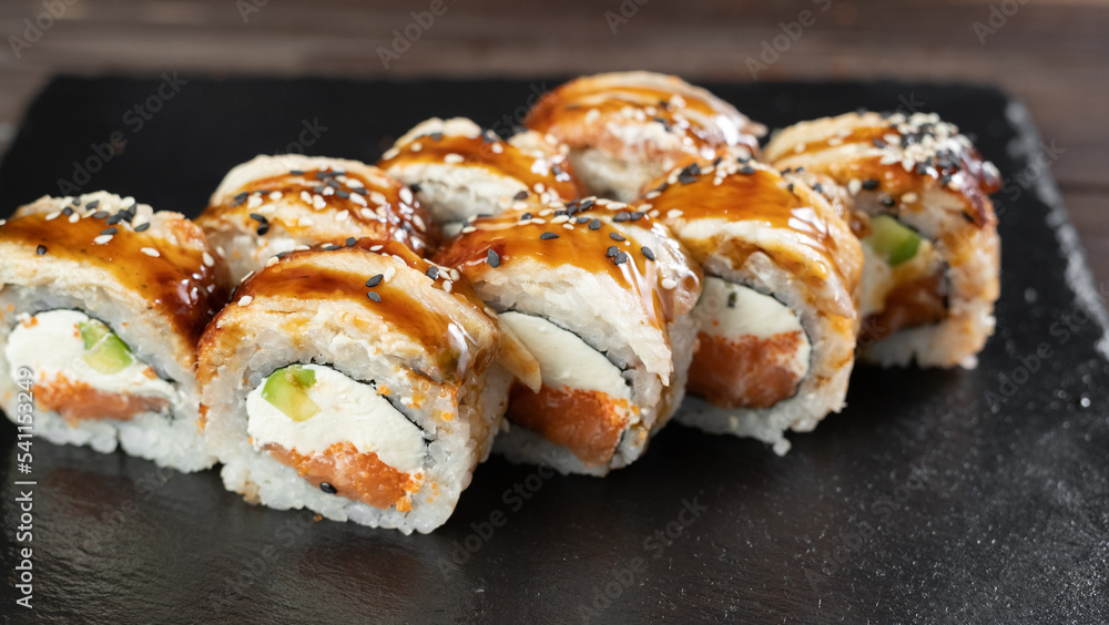 Delicious sushi roll topped with smoked eel and sesame seed. Sushi roll with avocado and crab meat. Black slate sushi plate. Delicious sushi restaurant menu Delicious sushi roll topped with smoked eel and sesame seed. Sushi roll with avocado and crab meat. Black slate sushi plate. Delicious sushi restaurant menu