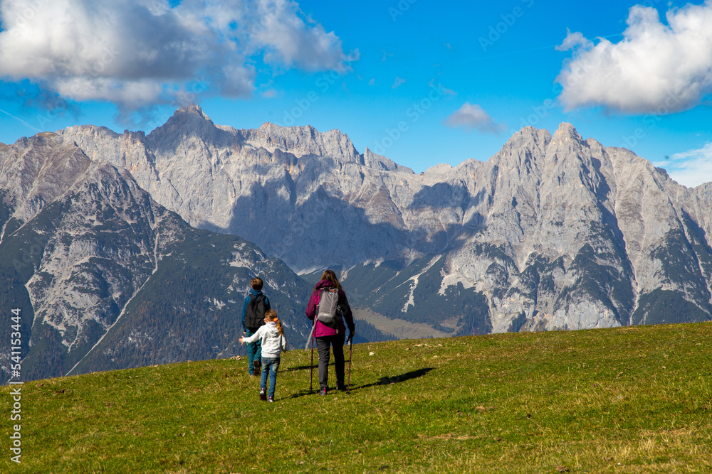 Wandern mit Kindern in Seefeld, Tirol: Familie wandert über eine Almwiese, im Hintergrund das Wettersteingebirge