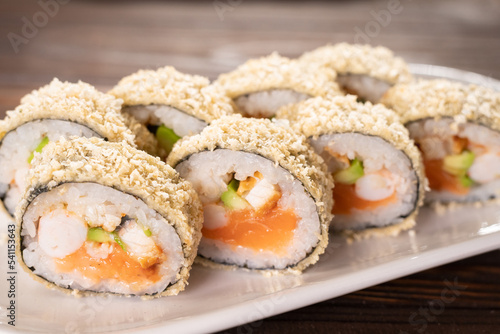 Japanese tempura hot sushi roll on white plate on wooden background. sushi pieces with salmon, cream cheese, avocado wrapped in rice with crunchy seaweed