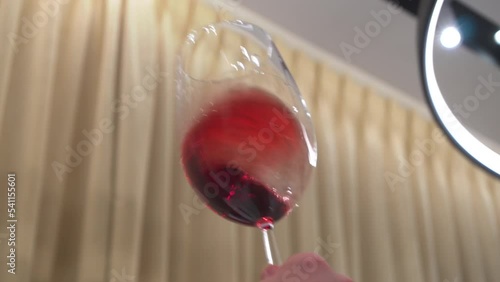 Wine degustation. Man swirling a wineglass on a long leg to inhale the aroma of red wine. Noble drink rotates and covers the walls of transparent goblet with reflections in a warm interior. 