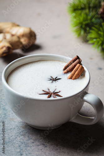 Homemade chai latte with cinnamon and star anise in white cup, dark background.