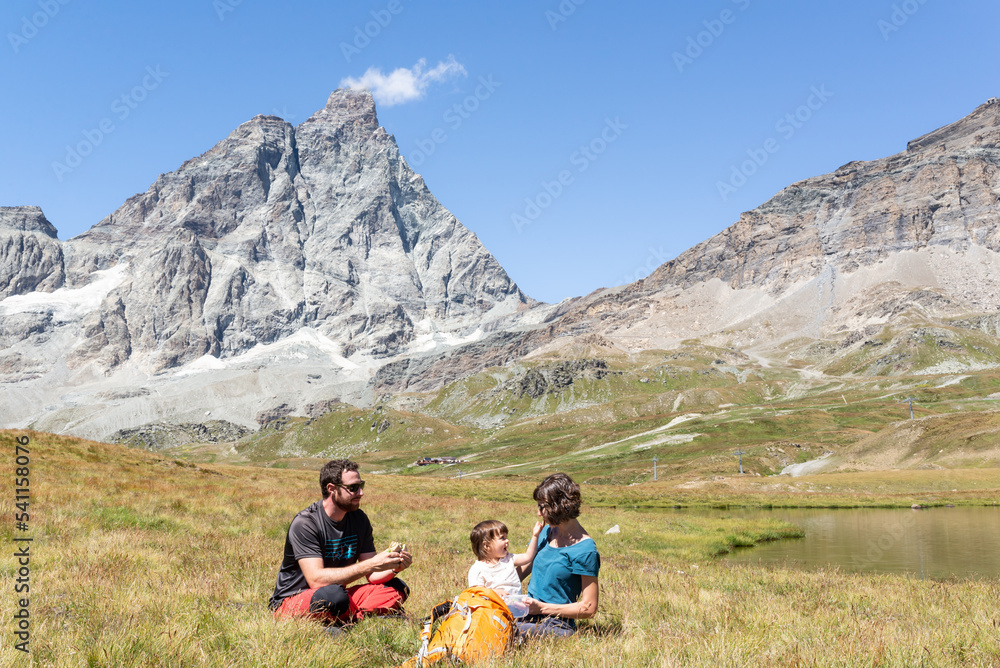 Fototapeta premium Couple with her little girl having a picnic close to a lake under the Matterhorn at italian alps.