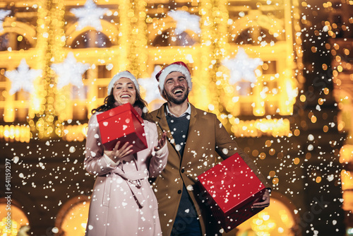 Young romantic couple is having fun outdoors in winter holding Christmas gifts.