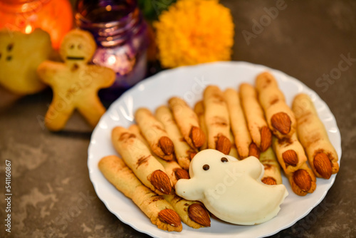 homemade cakes for halloween, cookies in the form of witch fingers on the background of marigolds, pumpkins and candles