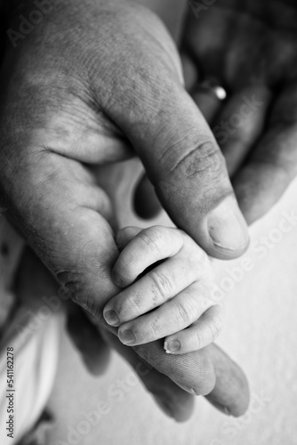 The hand of a sleeping newborn in the hand of parents, mother and father close-up. Tiny fingers of a newborn. The family is holding hands. Black and white macro photography Concepts of family and love © Vad-Len