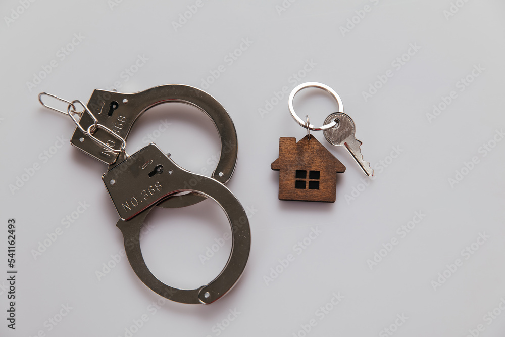 Handcuffs and house keys on a table. Real estate and fraud concept Handcuffs and house keys on a table. Real estate and fraud concept