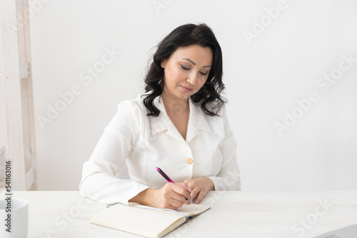Indian woman beautician takes notes in office - cosmetologist business woman or doctor concept