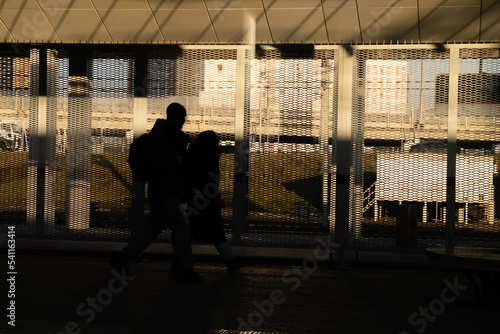 Male and female silhouettes in the shadows and without faces walk through the train station. Copy space