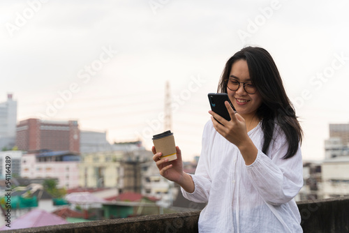 Happy woman using mobile phone smiling on the roof. Using a smartphone during a break, relaxing with coffee.