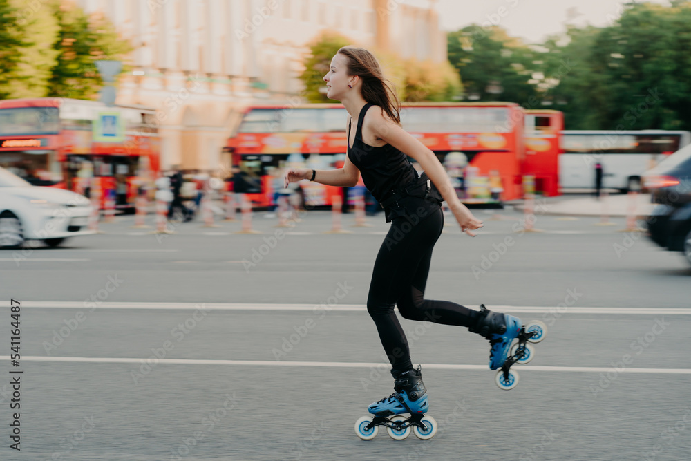 Outdoor activities for being healthy and fit. European woman in good physical shape rides on rollers rolleblades on inline skates dressed in active wear has active rest. Sporty lifestyle concept Outdoor activities for being healthy and fit. European woman in good physical shape rides on rollers rolleblades on inline skates dressed in active wear has active rest. Sporty lifestyle concept