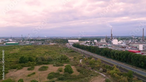 Fast flying drone towards an passenger tram on tracks to Sürth, Cologne, Germany - aerial bird view of an chemical industry plant in the background and a little forest green zone in the front 2022 photo