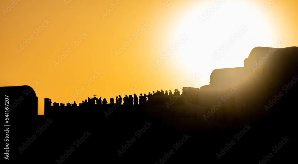 People silhouetted against an orange sky at sunset on the Greek island of Santorini