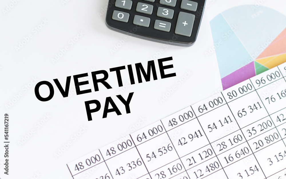 Overtime pay text on notepad on the table next to documents, charts Overtime pay text on notepad on the table next to documents, charts
