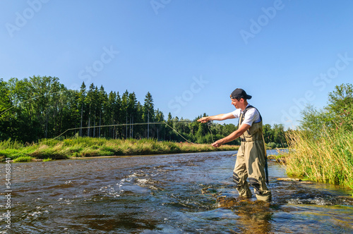 Fliegenfischer in Aktion in einer idyllischen Fluss-Landschaft an der Wertach in Schwaben photo