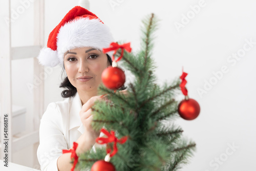 Closeup portrait Indian Christmas cosmetologist woman with Santa Claus hat and white dress - winter holiday season concept. Beautican office background